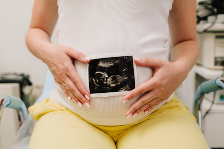 Pregnant woman holds an ultrasound photo of her baby on her tummy. Filming precious moments of motherhood with sonogramの写真素材