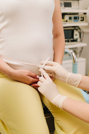 Gynecologist measures pregnant belly with measuring tape to follow the growth of the baby on the appointment. Gynecologist checks size of the woman belly in the clinicの写真素材