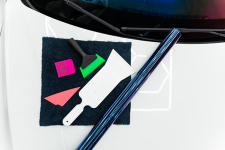 Iridescent purple tint film and installation tools on car hood in detailing workshop. Roll of purple...
