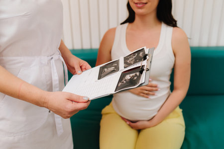 Gynecologist discusses the results of blood test of a pregnant woman. Consulting patient about high hemoglobin and blood pressure during pregnancy on the gynecologist appointmentの写真素材