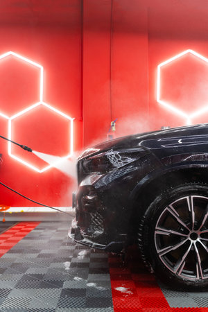 Car detailing process with high pressure water rinses dirt and foam from body panels and headlights leaving paint and glass spotless. High pressure water jet to remove dirt and foam from car bodyの写真素材