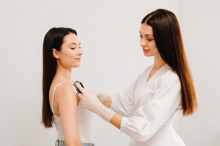 Dermatologist Examining Patient Shoulder with Dermatoscope. Dermatoscopic analysis aids in the detection of suspicious skin spots using dermatoscope during a clinical examの写真素材