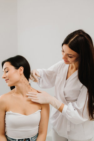 Cosmetologist is drawing dotes before botulinum toxin injection in platysma of girl. Nefertiti lifting injection in marked dotes on the neckの写真素材