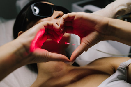 Laser coagulation procedure for nevus elimination and vascular lesion correction. Girl shows love to laser procedure using hands. Aesthetic laser therapy removes benign nevi and vascular lesionsの写真素材