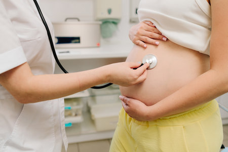 Pregnancy checkup. Gynecologist with stethoscope listening baby heartbeat in patient tummy on the appointment in gynecology clinicの写真素材
