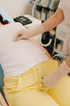 Gynecologist checks size of the woman belly in the clinic. Gynecologist measures pregnant belly with measuring tape to follow the growth of the baby on the appointmentの写真素材
