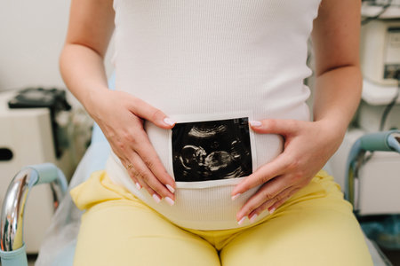 Filming precious moments of motherhood with sonogram. Pregnant woman holds an ultrasound photo of her baby on her tummyの写真素材