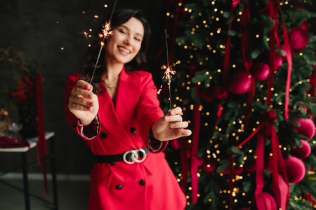 Cheerful woman with burning sparkler near Christmas tree enjoying New Year holiday