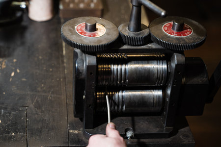 Jeweler drawing gold through rolling mills to produce wire or thin strips