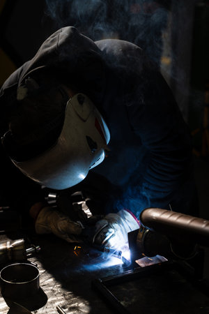 Industrial SMAW welding creating sparks on steel with protective helmet