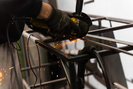 Industrial worker uses angle grinder to cut metal with safety helmet on