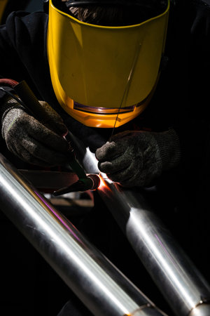 Welder TIG welds automotive exhaust pipe with argon and tungsten electrode