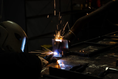 Flux-cored electrode SMAW welding by worker in protective helmet