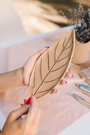 Young woman carves delicate leaf patterns into clay, showcasing her pottery skills. Artisan engraves...