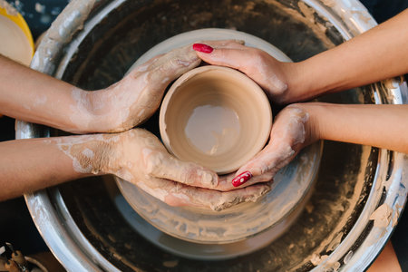 Teaching of shaping clay into a smooth ceramic vessel with precision. Two pairs of hands work...