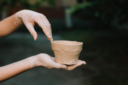 Finished clay pot in hands. Handmade clay bowl is held after removal from the wheel. Ceramic pot reflects artistry, patience, and cultural traditionの写真素材