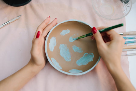 Hand painting ceramic bowl with blue design using pigment and brush. Painting ceramic bowl with blue pigment using brush. Ceramic bowl decoration highlights painting process and pottery techniqueの写真素材