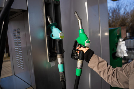 Hand holding gasoline nozzle at fuel station close-up. Driver refueling car using gasoline pump