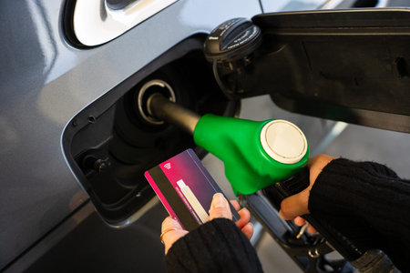 Hand holding bank card near gasoline nozzle during refueling