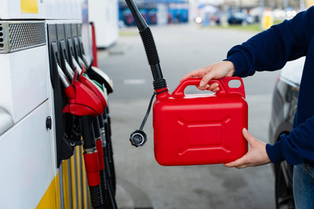 Hand gripping plastic fuel container near gas pump at station