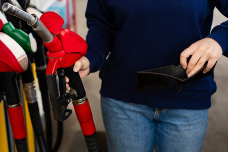 Hand holding gasoline nozzle at fuel station close-up