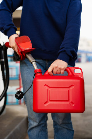 Fuel pump nozzle pouring gasoline into red plastic canister at gas stationの写真素材