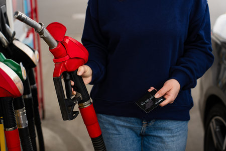 Hand holding bank card near gasoline nozzle during refueling