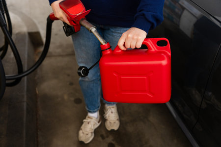 Refueling red plastic fuel canister with gasoline pump nozzle
