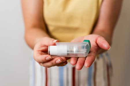 Close up of hand holding inhaler on white background