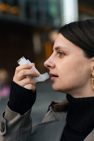 Female patient using asthma inhaler for respiratory relief outdoors