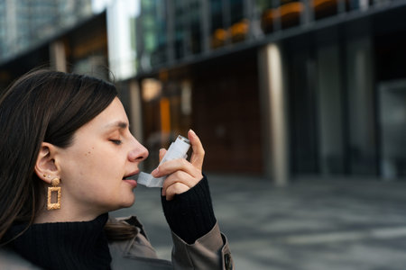 Young woman spraying asthma inhaler and inhaling medication outdoors