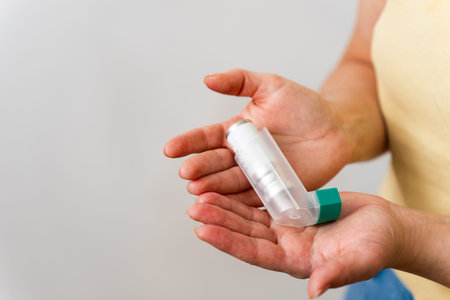 Close up of hand gripping asthma inhaler on white background