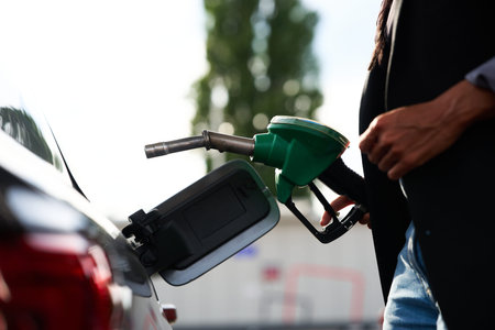 Detailed view of a hand utilizing a green fuel nozzle to pump gasoline into a car at a modern petrol station location