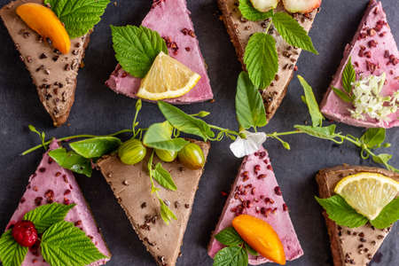 Appetizing pieces of raw mousse cakes, decorated with fruits, berries, flowers and green leaves....