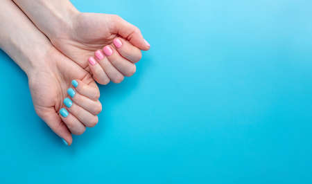 Women's hands with bright summer manicure on a blue background. Fashionable colors of nail polishes for young women. Copy spaceの写真素材