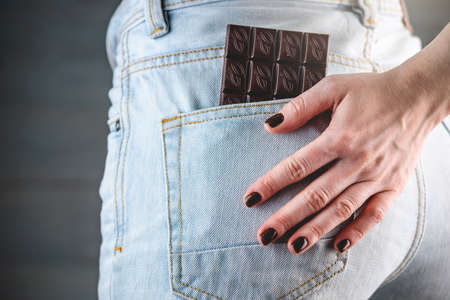 A woman's manicured hand with brown nail polish is located on the back pocket of light jeans, from...