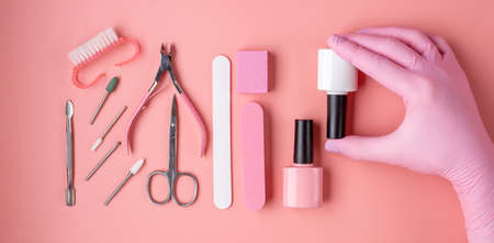 A set of tools for manicure and pedicure in white and pink on a pink background. A woman's gloved...