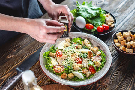 The chef is grating the cheese into an appetizing fresh salad. Concept of cooking delicious Caesarの写真素材