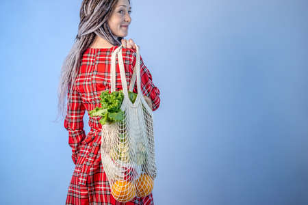 A modern woman with dreadlocks is carrying shopping in a string bag. Concept of eco-friendly behavior, the use of reusable bags and care for the environment. Copy spaceの写真素材