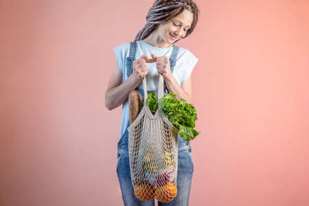 A modern woman in jeans is holding a string bag with purchases. Concept of eco-friendly behavior,...