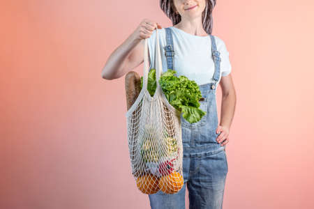 A modern woman in jeans is holding a string bag with purchases. Concept of eco-friendly behavior,...