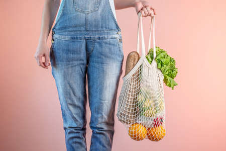 A modern woman in jeans is holding a string bag with purchases. Concept of eco-friendly behavior,...