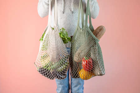 A modern young man is holding a string bags with purchases. Concept of eco-friendly behavior, the use of reusable bags and concern for the environmentの写真素材