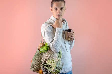 A modern young man is carrying a string bags with purchases. Concept of eco-friendly behavior, the use of reusable bags and concern for the environment. Pink backgroundの写真素材