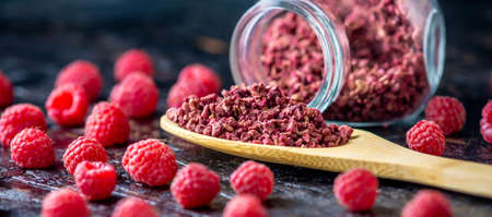 Freeze dried raspberries in a glass jar and a wooden spoon on a black background. Concept of berry...
