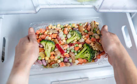 Hands are taking a container of frozen vegetables from the freezer of the fridge. Concept of storing ready dish and saving time.の写真素材