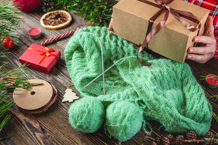 Woman is holding a gift box in her hands and a cozy warm sweater is knitted on the table. Concept of creating handmade gifts for New year and Christmas.の写真素材