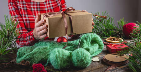 Woman is holding a gift box in her hands and a cozy warm sweater is knitted on the table. Concept of...
