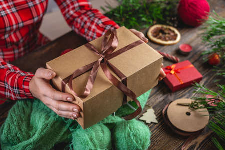 Woman is holding a gift box in her hands and a cozy warm sweater is knitted on the table. Concept of...