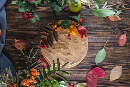 Brown mousse cake decorated with autumn leaves and berries. Wooden background. Concept of autumn mood and atmosphere.の写真素材